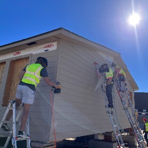Three students work on the exterior of a newly constructed house.